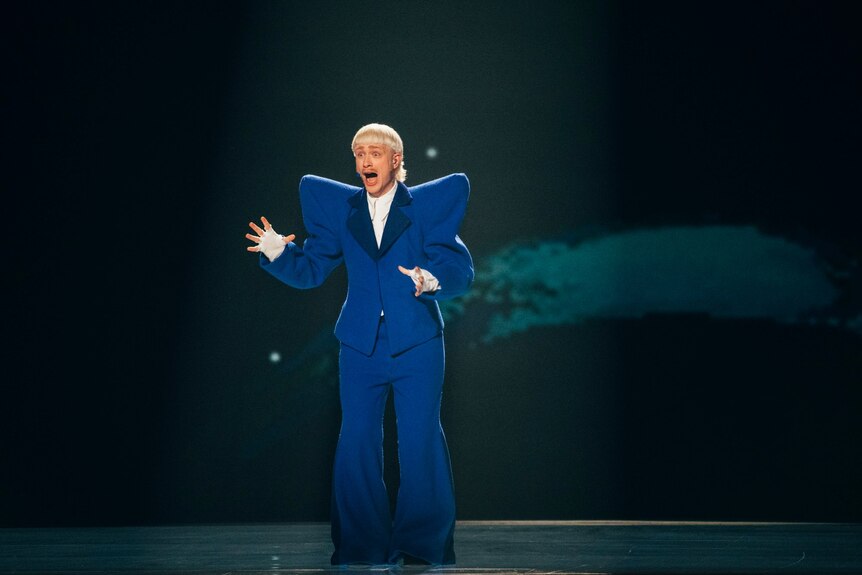 Joost Klein singing on stage with arms out and a blue blazer with exaggerated shoulder pads