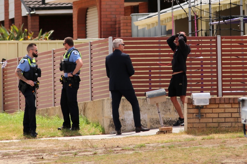 A man with his hands on his head, looking distraught, talks to a suited man with two police offcers nearby