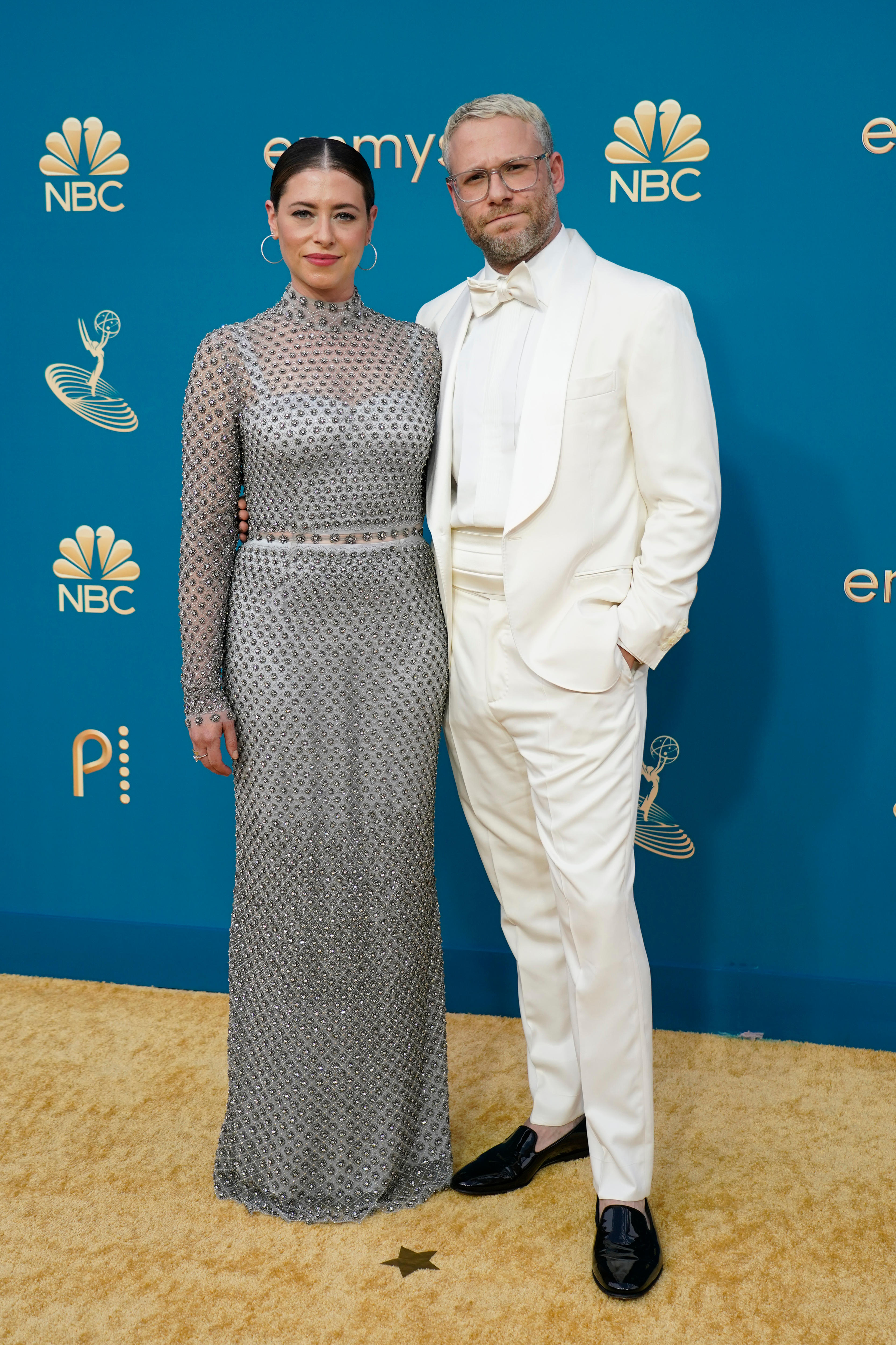 Lauren Miller wears a long-sleeved silver dress and Seth Rogen wears a white suit.