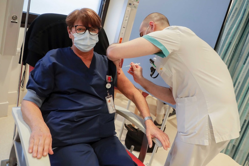 A woman wearing a facemask receives a coronavirus vaccine