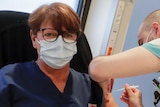 A woman wearing a facemask receives a coronavirus vaccine
