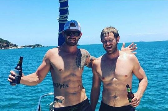 James and Ben Cullen holding beers standing on a fishing boat off the coast