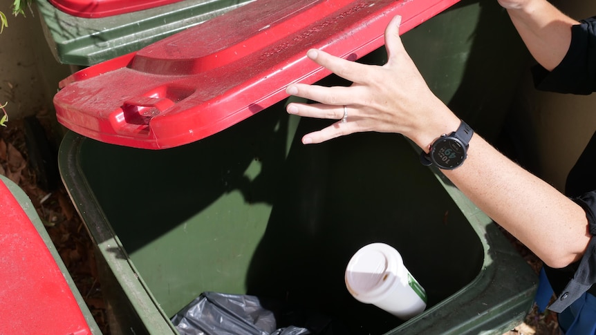 A hand letting go of a compostable disposable coffee cup in a landfill bin