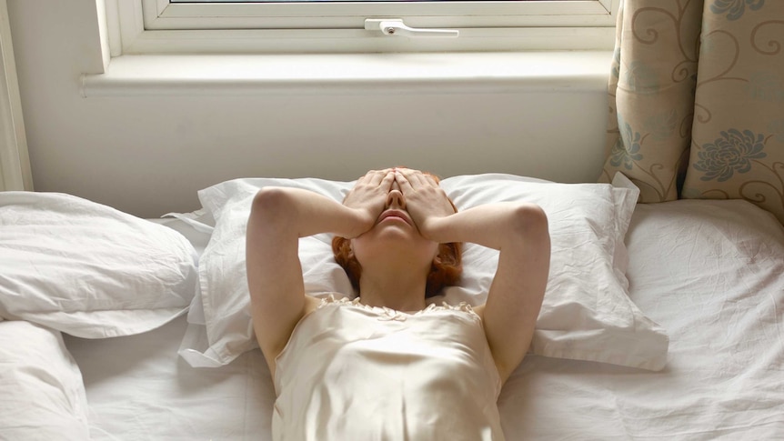 Woman on bed with hands over eyes.