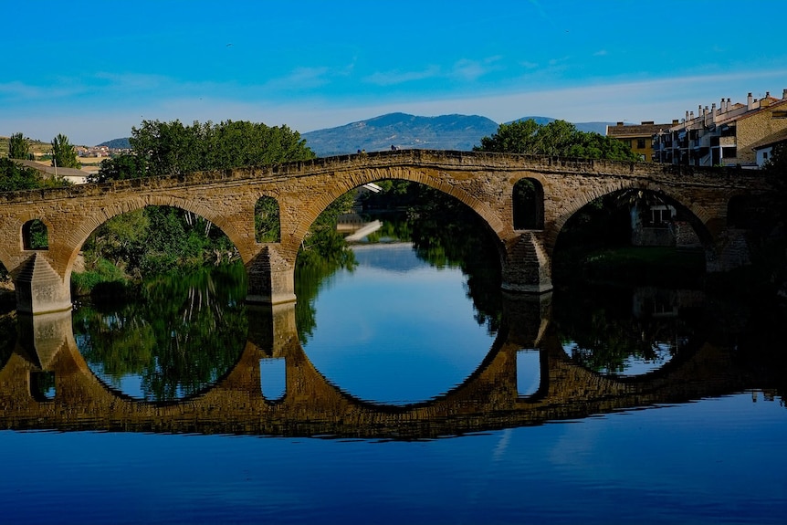 在晴朗的日子里，运河上的一座桥反映了蓝天和山脉的美丽艺术形象