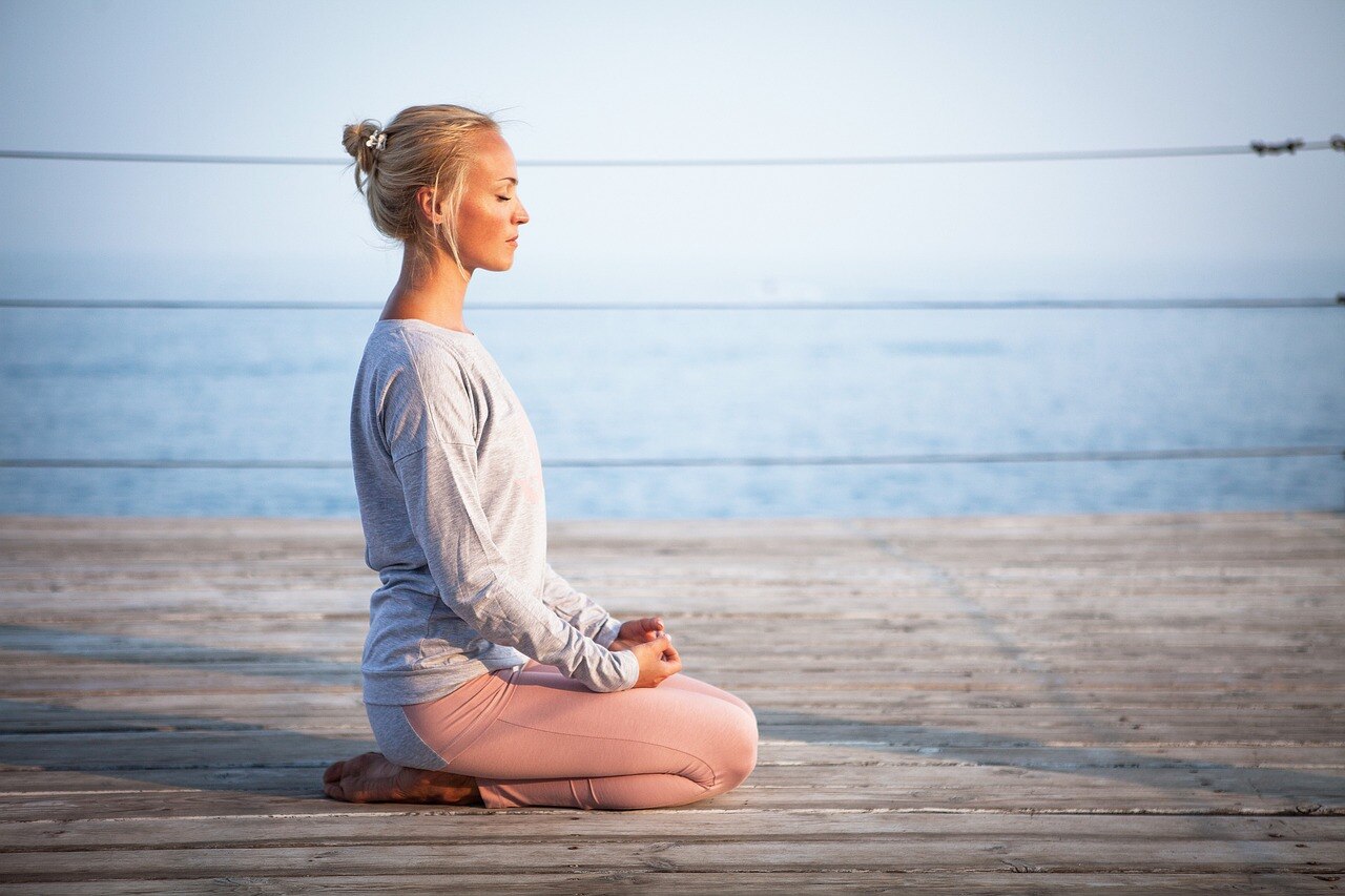 A woman sits on a jetty, with her eyes closed. The ocean is in the background