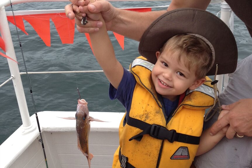 A young boy holding a small fish.