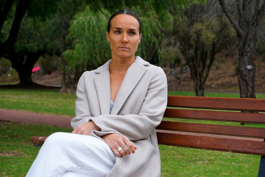 A woman wearing a grey coat in a park looking serious. 