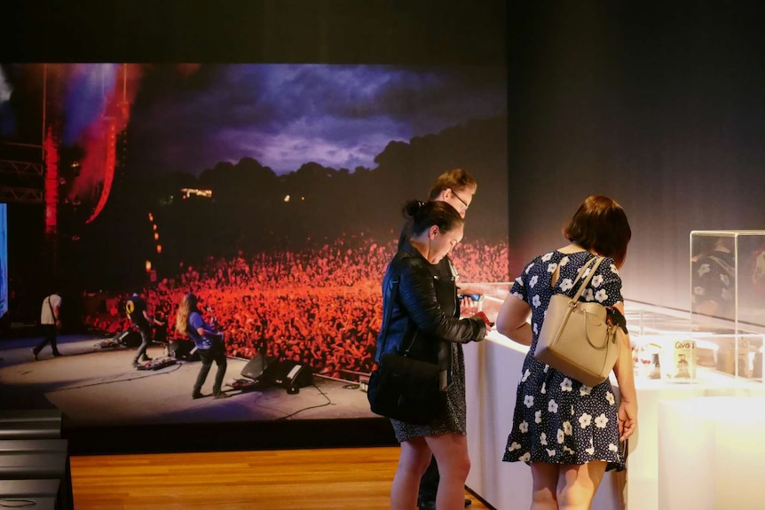 People looking into display cabinets near a music poster.