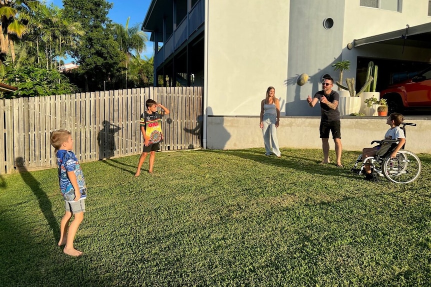 Zane Warrell about to catch a football that is in the air as his kids and wife stand around in the backyard.