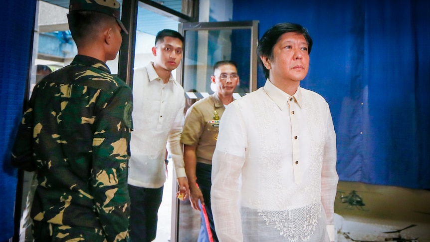 Ferdinand Bongbong Marcos Jr in an embroidered white shirt, walks into a room surrounded by military 