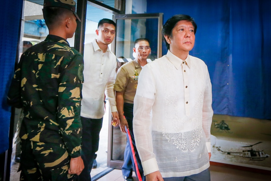 Ferdinand Bongbong Marcos Jr in an embroidered white shirt, walks into a room surrounded by military 