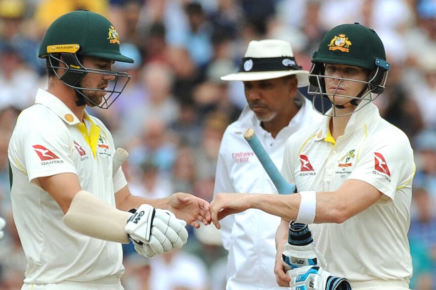 Australia batsmen Travis Head (left) and Steve Smith touch hands during a Test, while umpire Joel Wilson watches on.