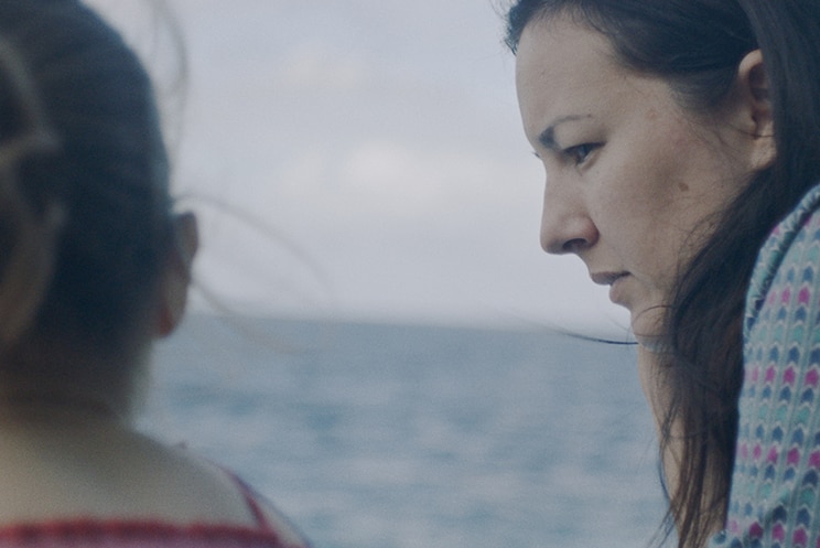 Colour still of Poh Lin Lee with daughter sitting by the ocean in 2018 film Island of the Hungry Ghosts.