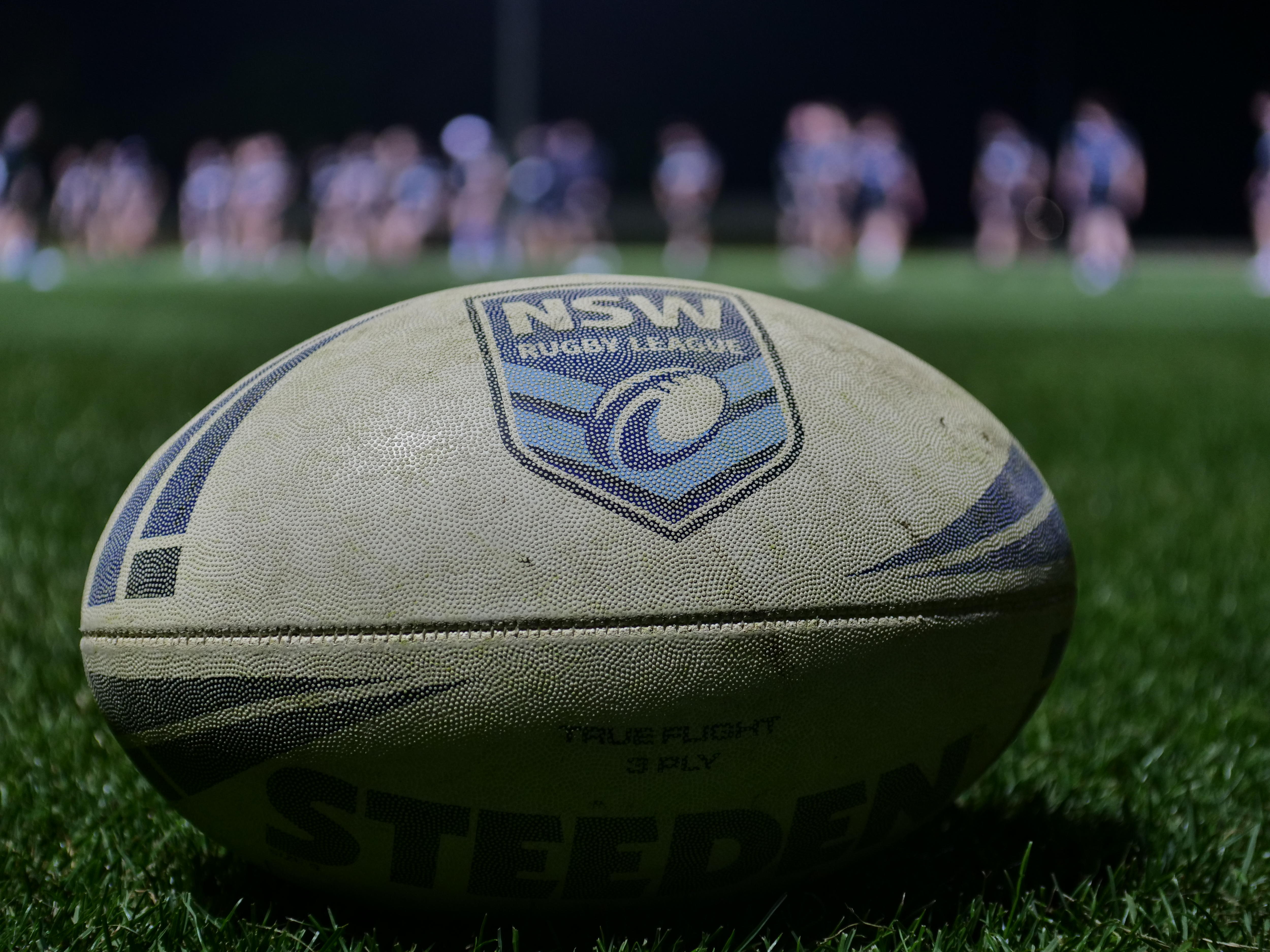 A rugby league football resting on the grass at a sporting field
