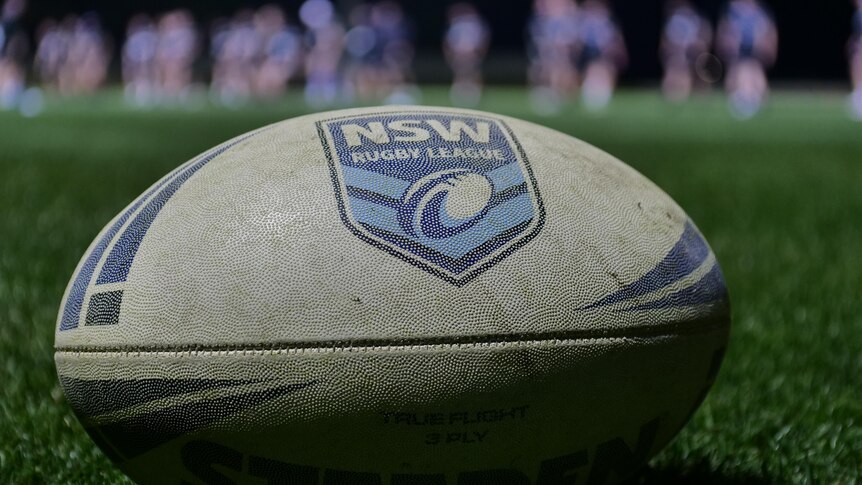 A rugby league football resting on the grass at a sporting field