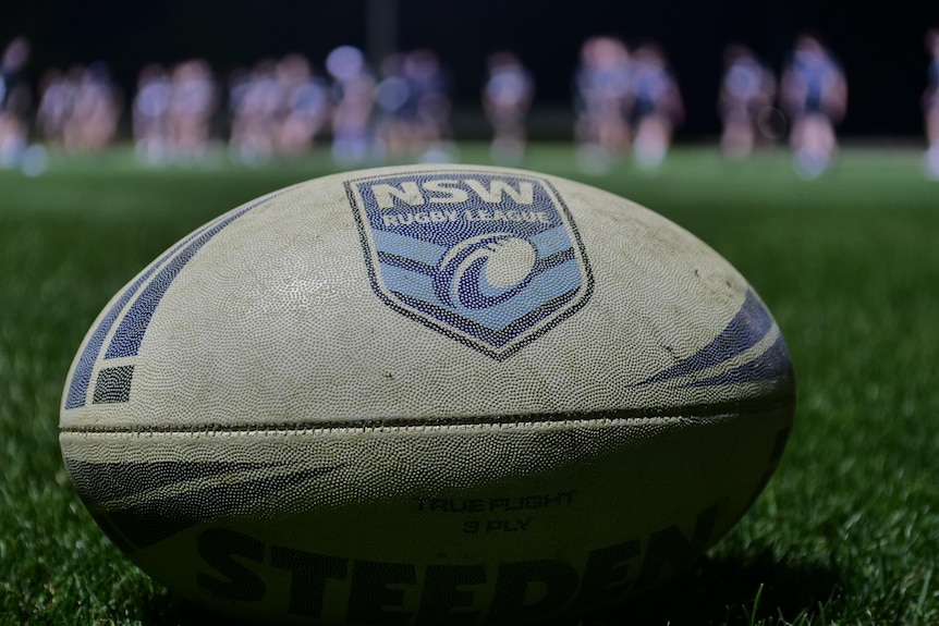 A rugby league football resting on the grass at a sporting field