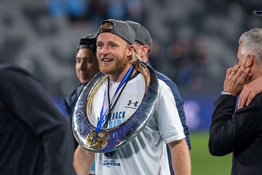 Rhyan Grant, wearing a grey cap and white shirt, wears the A-League trophy round his neck
