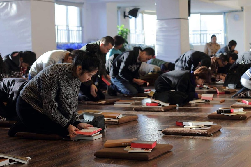 Worshippers at the Early Rain Covenant Church in Chengdu pray on the floor, bowing with bibles and pillows.