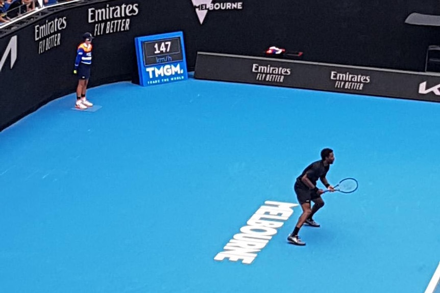 tennis player dressed in black waiting for serve with ball kid in corner