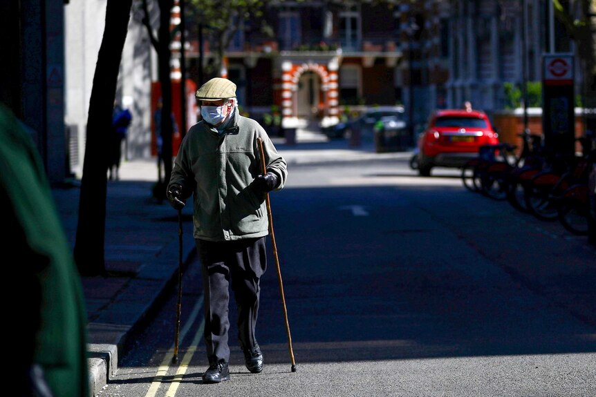 An elderly man with two walking sticks in a face mask