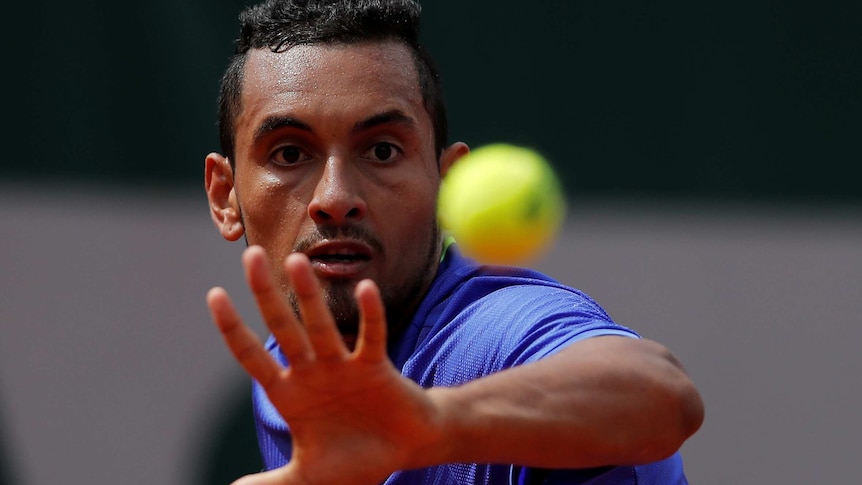 Nick Kyrgios focuses on a tennis ball as he serves during the French Open.