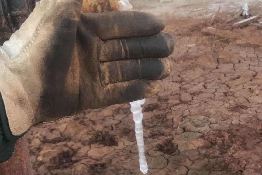 A gloved hand in front of a water pipe with a block of ice coming out of it.