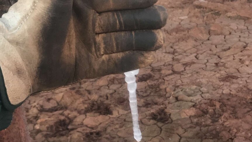 A gloved hand in front of a water pipe with a block of ice coming out of it
