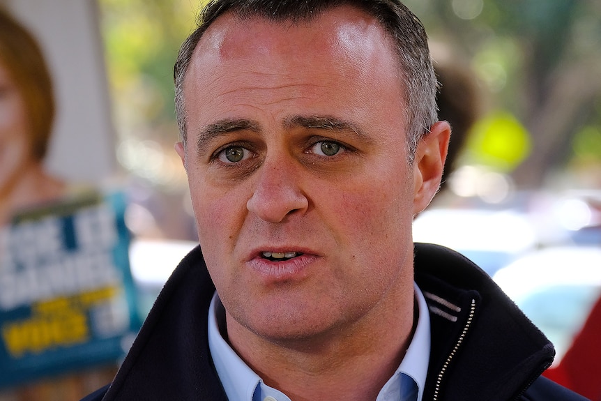 Tim Wilson talks to the media in front of a campaign sign for his challenger Zoe Daniel