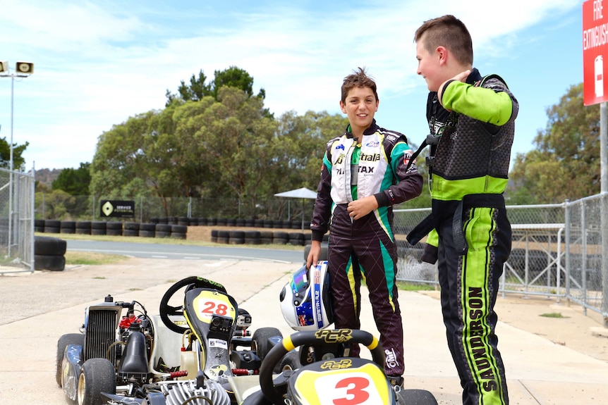 Two boys stand next to their karts just off a track.
