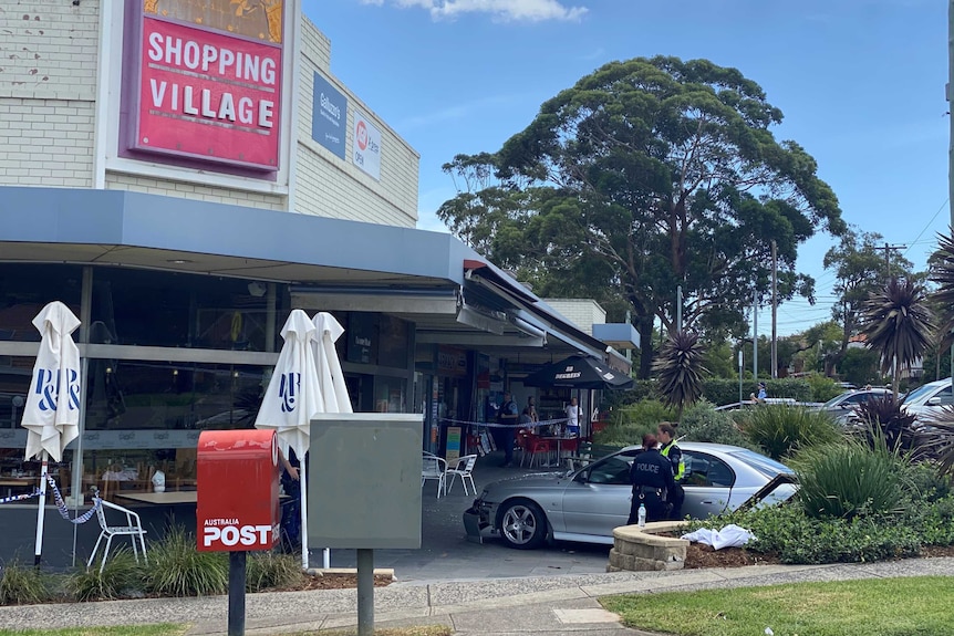 Car with damage to its front is seen in front of cafe, police stand nearby.