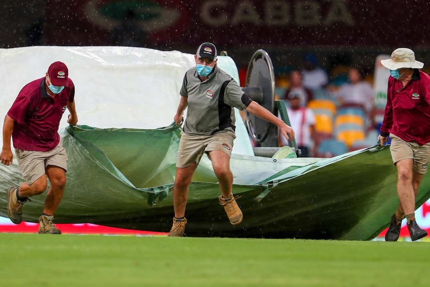 Ground staff bring covers onto the field at the Gabba as rain falls