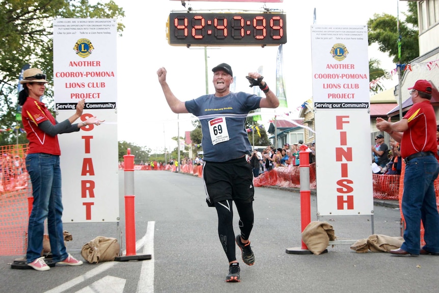 A man in running clothes is cheered on as he crosses the finish line of a race