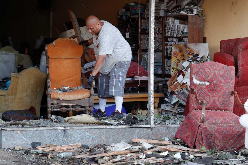 A man sweeps out debris from a damaged building