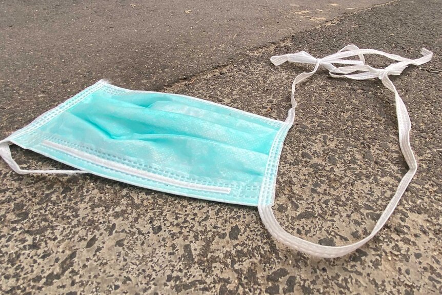 A blue surgical mask with ties disposed of on the ground.