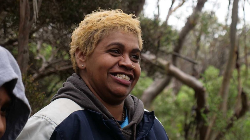 A woman with short blonde hair laughs and smiles at something off screen.