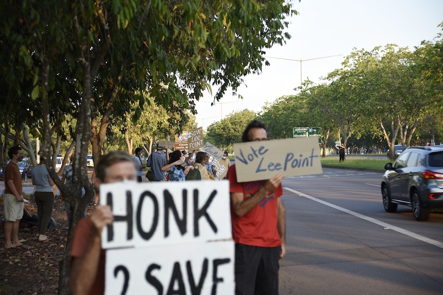 Community members in Darwin hold protest signs to save Lee Point.
