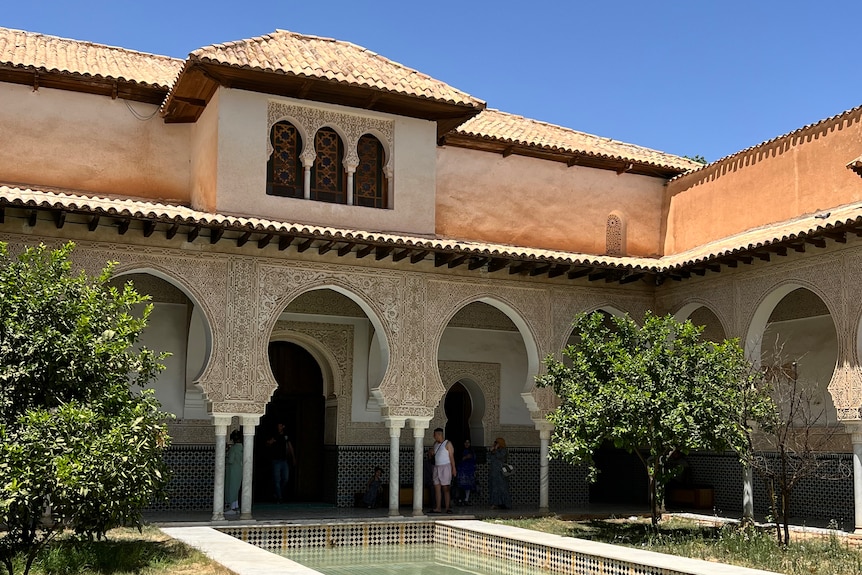Un palacio con un intrincado exterior de azulejos frente a una piscina de azulejos poco profunda.