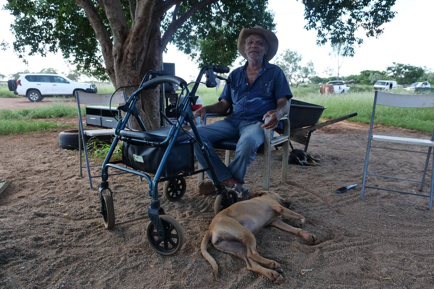 an older man sits on a chair next to a dog outside a home
