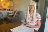 A grey-haired lady sits at a table with paperwork
