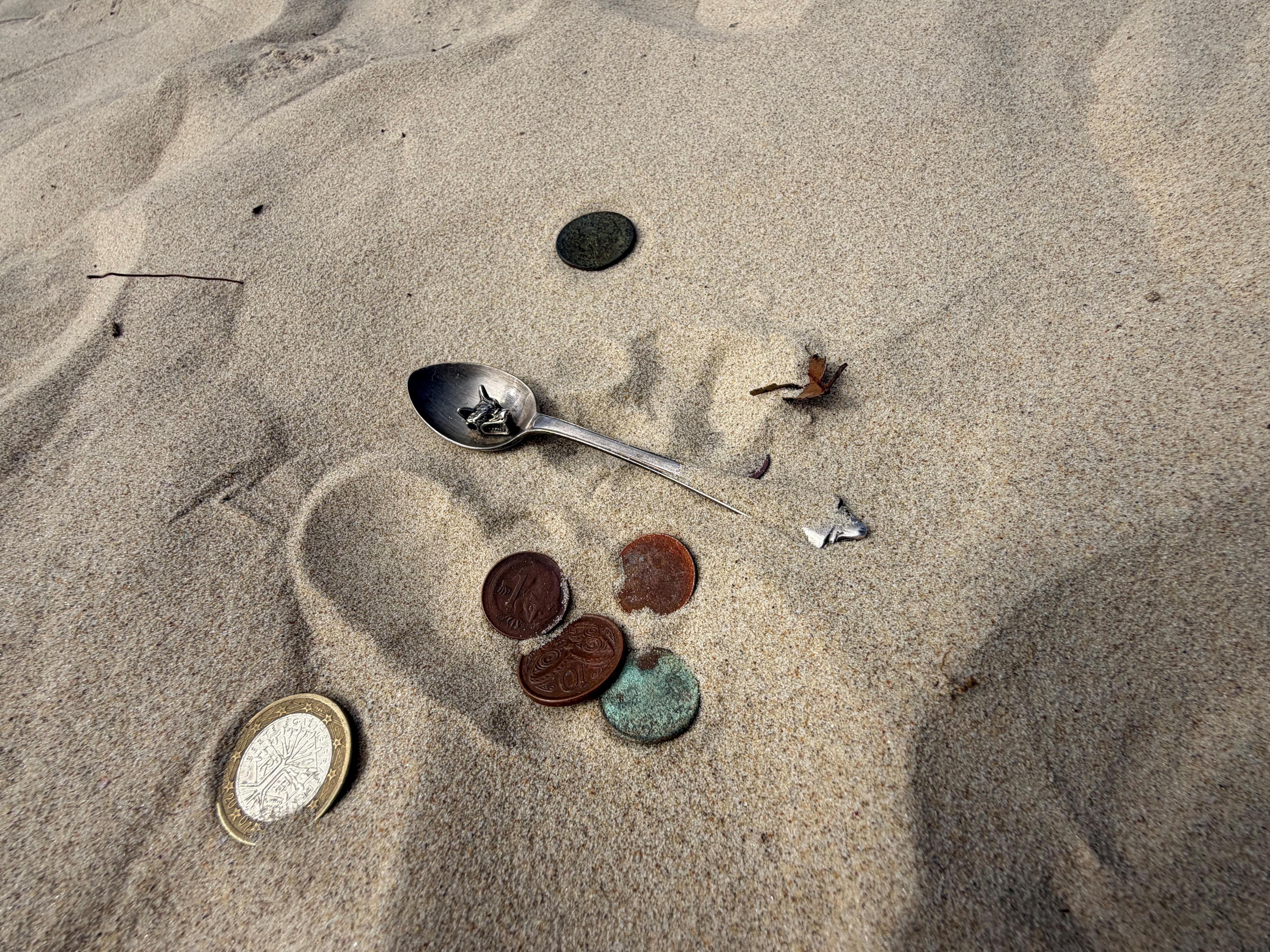 Uma coleção de moedas e uma colher de chá na areia da praia.