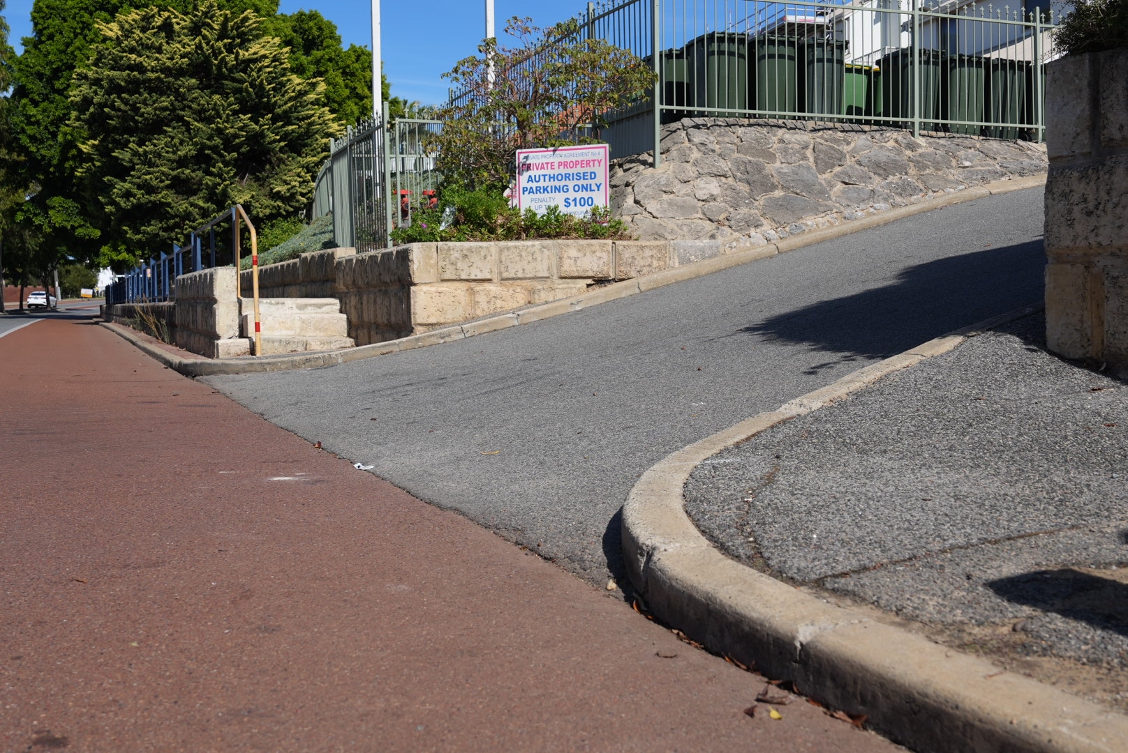 A close-up shot of a short drive way sloping up to enter a car park from a residential street, with a 'private property' sign.