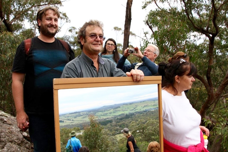 Kim Leevers holds a mirror to reflect the sun to create a flash to be seen in Katoomba