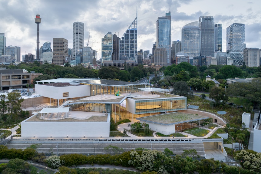 A building with many glass windows over three levels, painted white, is in the foreground, with the Sydney skyline behind