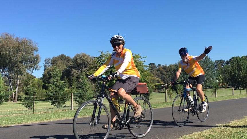 An older man and woman riding bikes along a country road