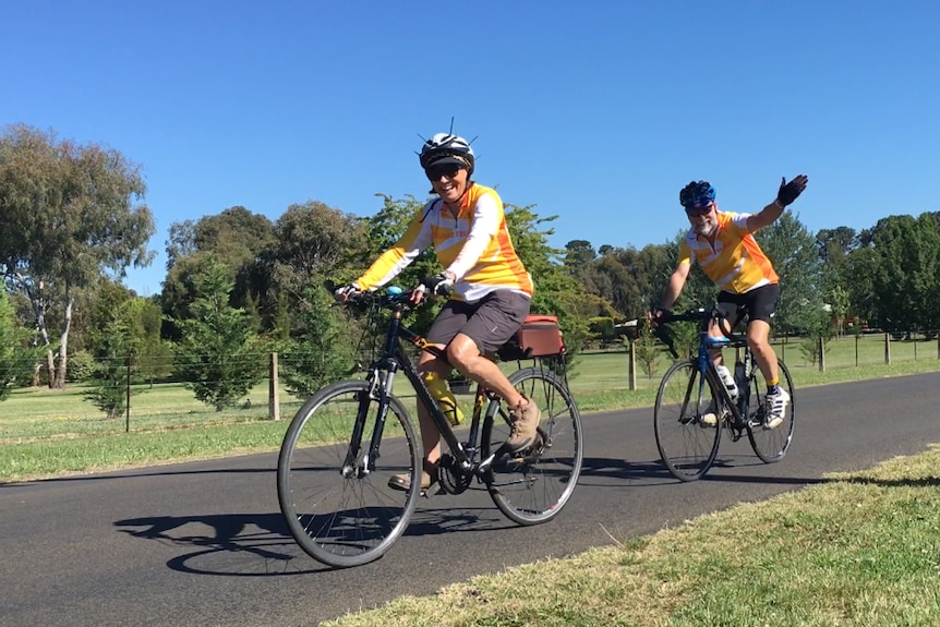 An older man and woman riding bikes along a country road