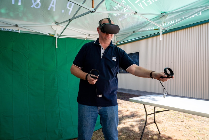 A man wears big virtual reality googles on his head and waves remote controls in hands.