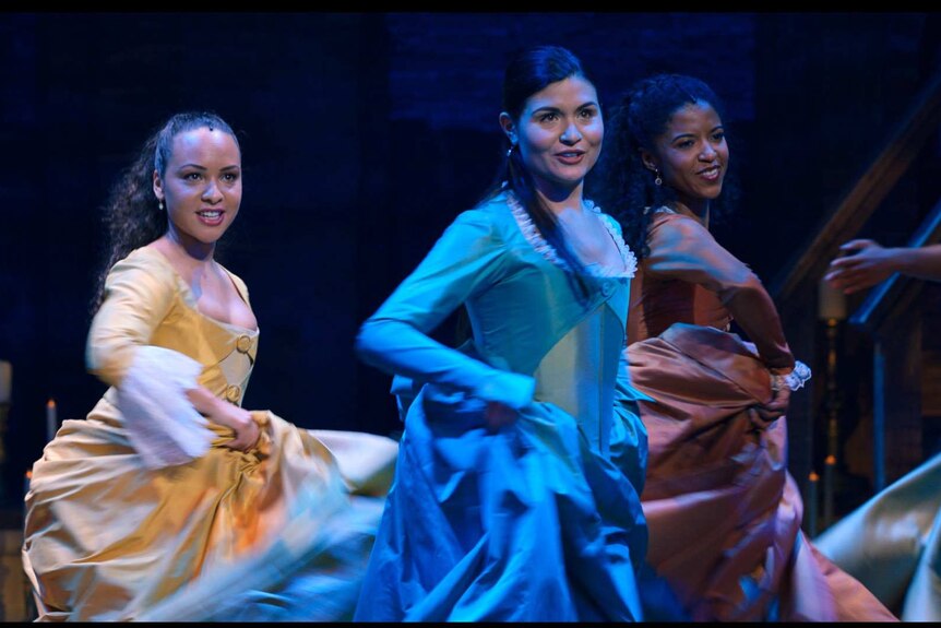 The three actors twirl their colourful dresses as part of a choreographed dance