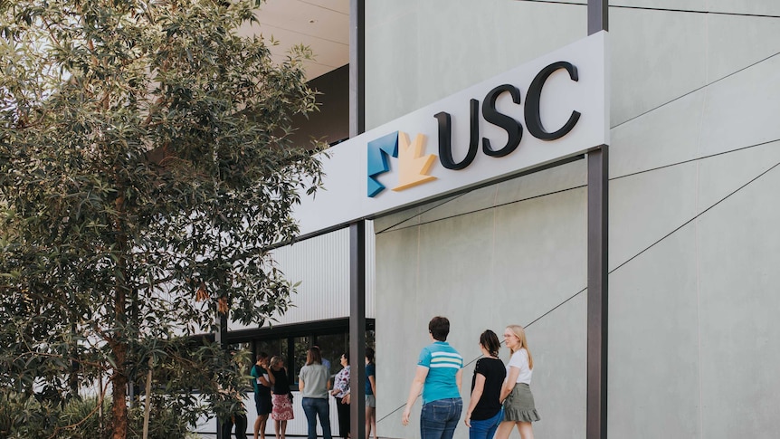 Students walk into a USC Gympie building under the university's sign.