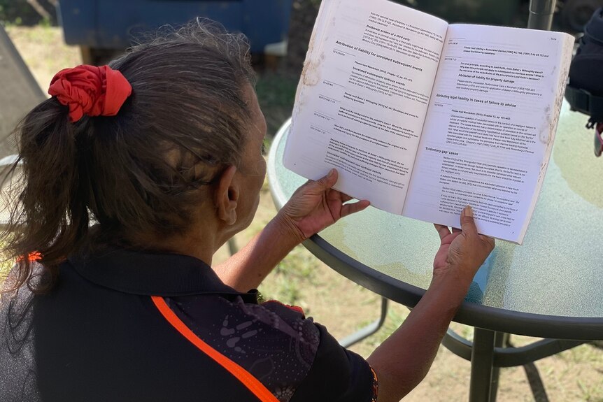 An Indigenous woman sitting with her back to the camera, hair in ponytail, reading a textbook.